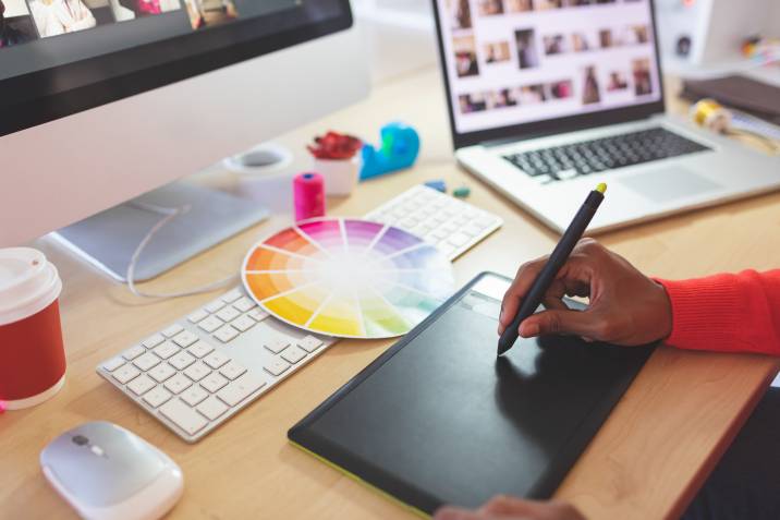 Young woman drawing on graphic tablet at desk. Graphic design side hustle from home