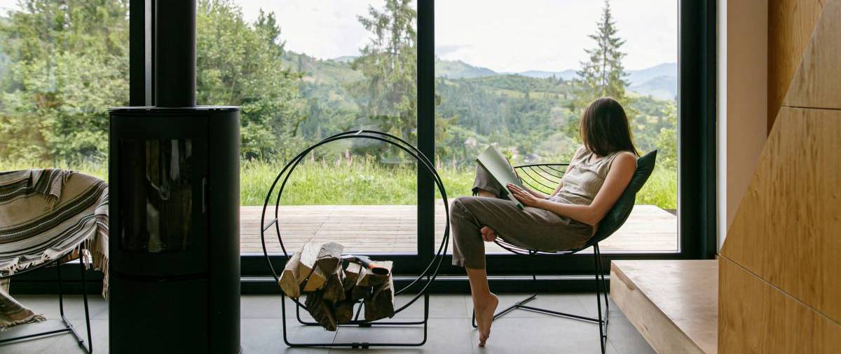 woman reading book on chair by a window with mountain view, house sitting, easy side hustle