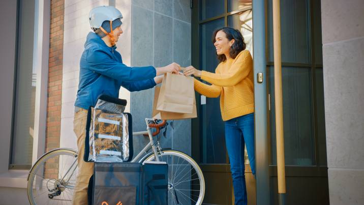 happy food delivery man on a bike delivering restaurant order to a customer to earn extra money during spring