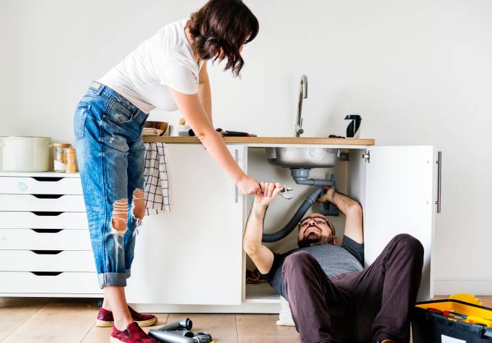 Home repair. Couple fixing someone's kitchen sink to earn extra money. Woman passing a wrench to her boyfriend fixing the sink