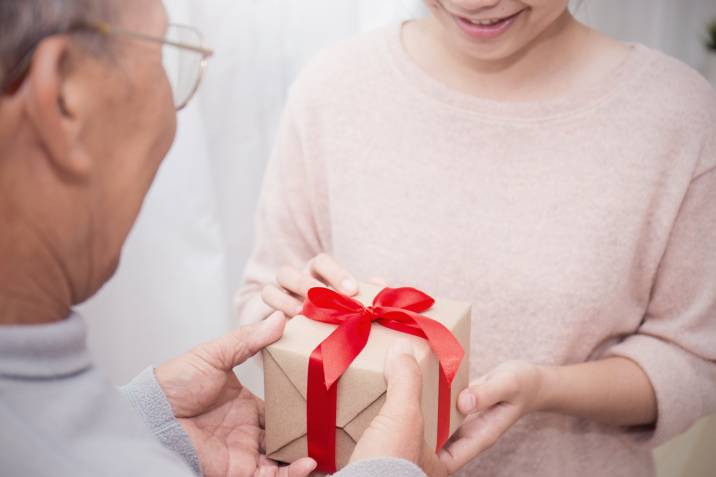 senior man delivering a gift to a smiling young lady, part-time job for retirees 