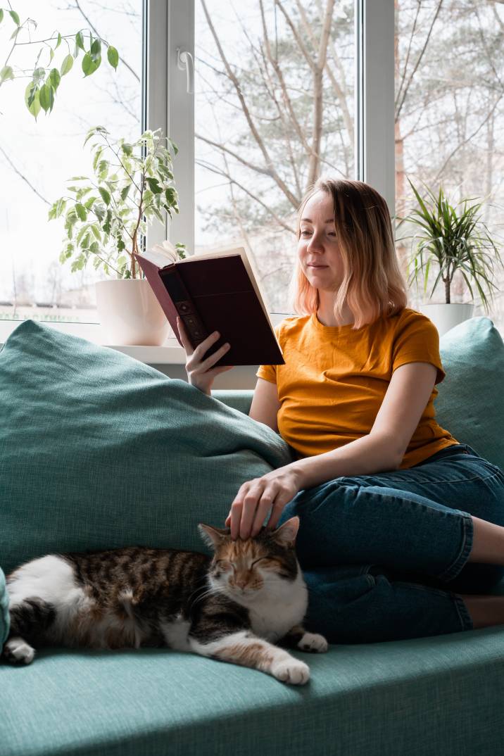 stay-at-home mom reading book on sofa and petting cat, pet sitting side hustle