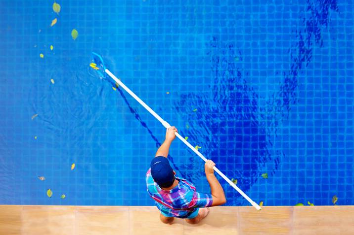 top view man cleaning pool, removing fallen leaves on a summer day