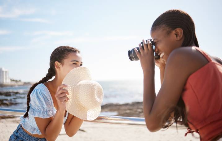 Woman photographer and model girlfriend at the beach in summer shooting creative, happy pictures. Taking photos for a small business to use on social media