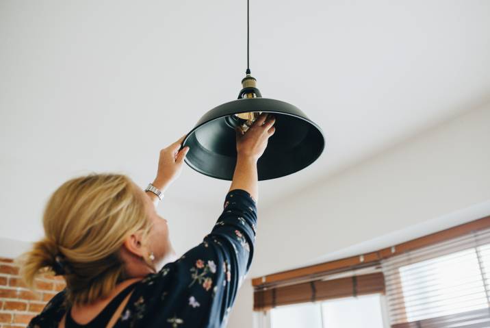 Woman changing a light bulb hanging from the ceiling