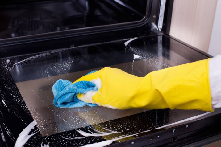 Closeup female hand with yellow protective gloves, cleaning oven door, cleaning side job