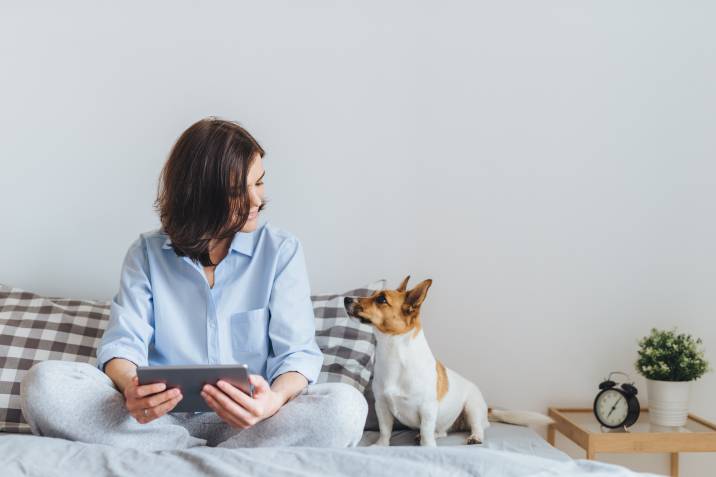 Beautiful brunette woman in pyjamas sitting on bed with jack russell terrier dog, pet sitting side hustle for single moms