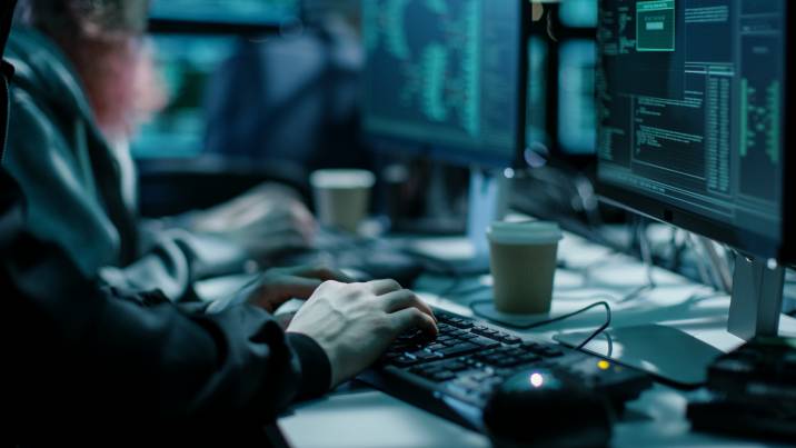 Close-up shot of hacker using keyboard, coffee cup and computer monitor with various information