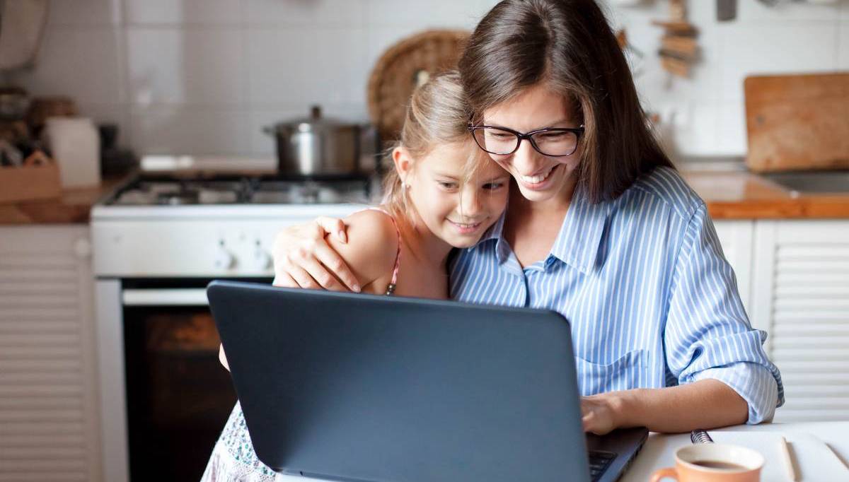 Mom working from home office with kid. Hugging child while working on laptop