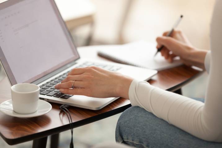 Woman virtual assistant working on laptop and writing on notebook 