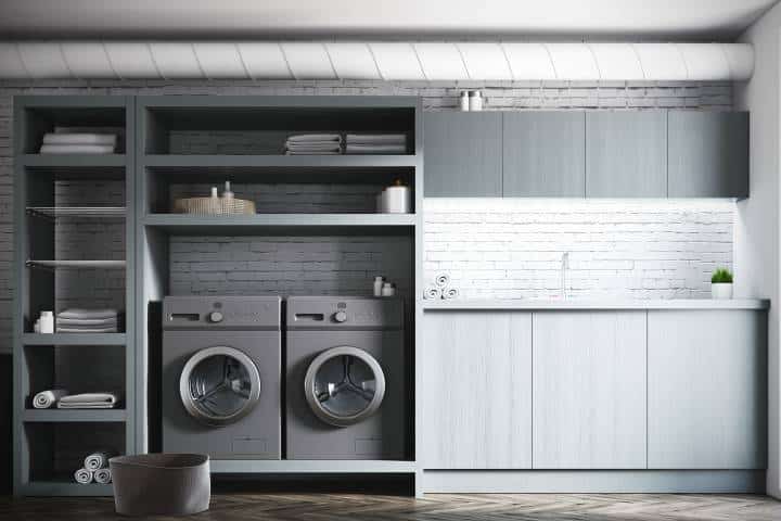 laundry area with grey cabinets and white brick walls