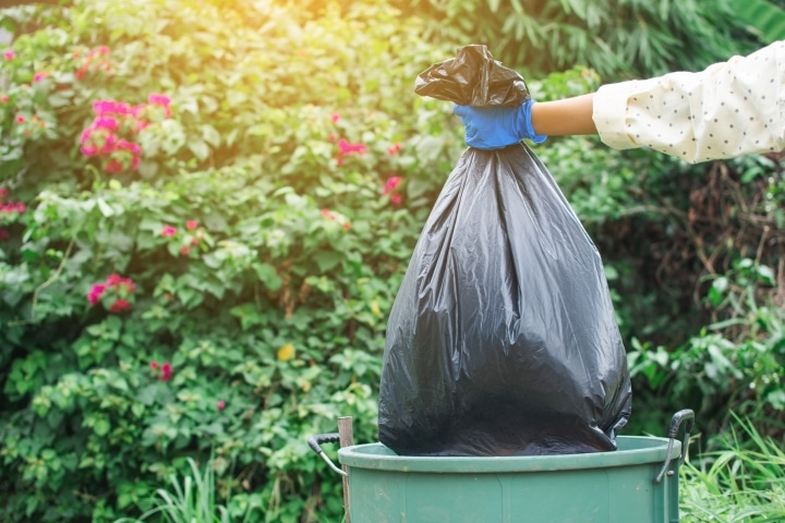 a woman holding a garbage bag above a bin