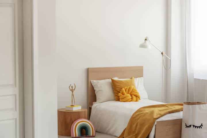 White and yellow bedding on single wooden bed in contemporary hotel interior