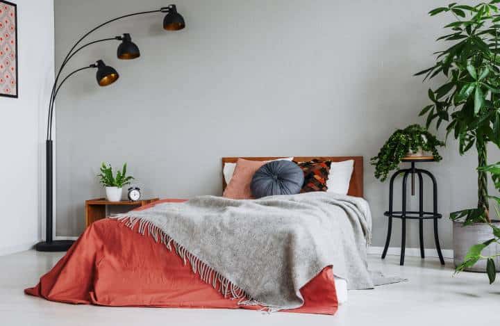 Grey blanket on red bed with cushions in bedroom interior