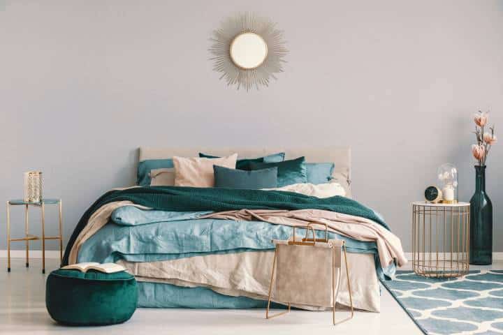 Blue, beige and emerald green bedding on king size bed in contemporary bedroom interior with golden accents