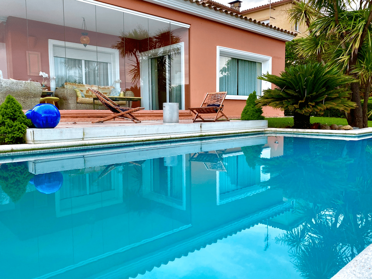 Pool house with orange exterior wall and floor-to-ceiling window. Two folding chairs beside pool