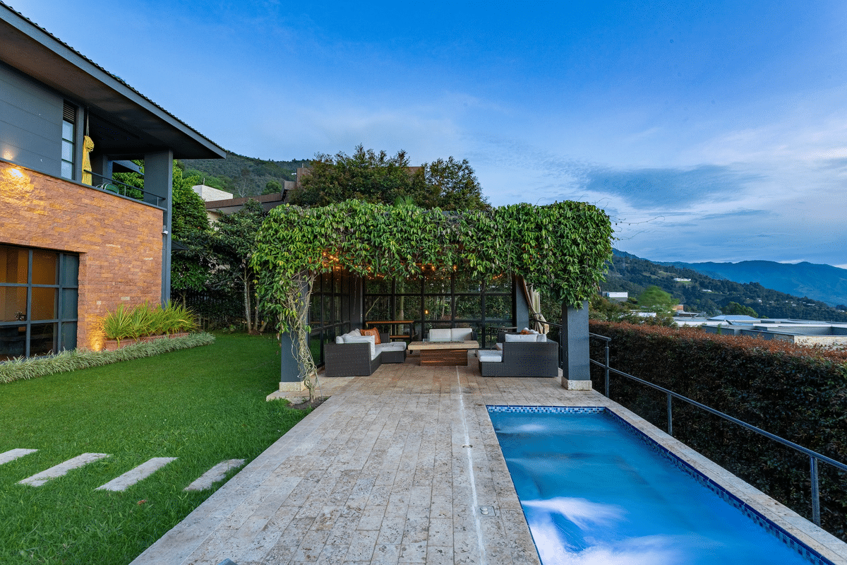 pool next to outdoor terrace with glass walls and overgrown plants