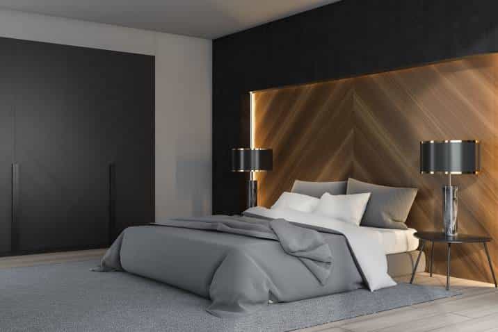 Modern bedroom with lighting feature on accent wall. Black, white and wooden luxury bedroom interior with double bed standing on grey carpet and two lamps on bedside tables