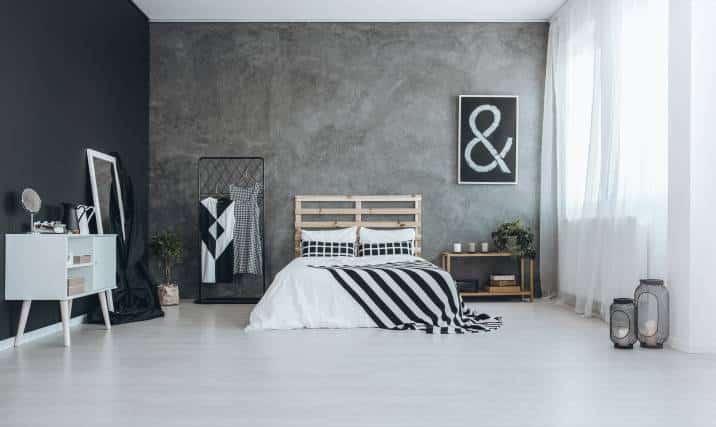 Black, white, and grey modern bedroom. Concrete wall, two black and white dresses on hanger, black and white bedding and ampersand wall art 