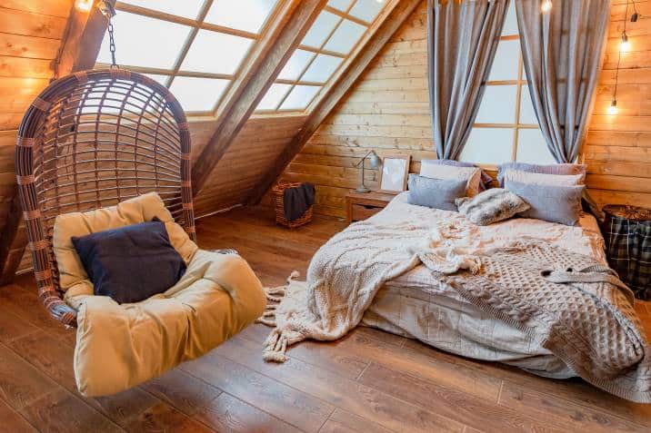 Cosy bedroom with indoor swing with pillow and seat cushion. Country house in a wooden design with large windows