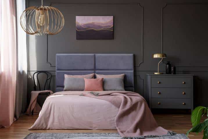 Gold lamp on grey cabinet next to pink bed in elegant pastel bedroom with chair