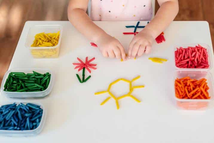 Little girl making art with painted pasta 