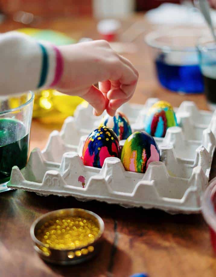 Child sprinkling glitter on coloured eggs on palette tray 