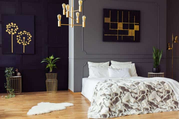Gold chandelier above bed in grey bedroom interior with black posters and plants