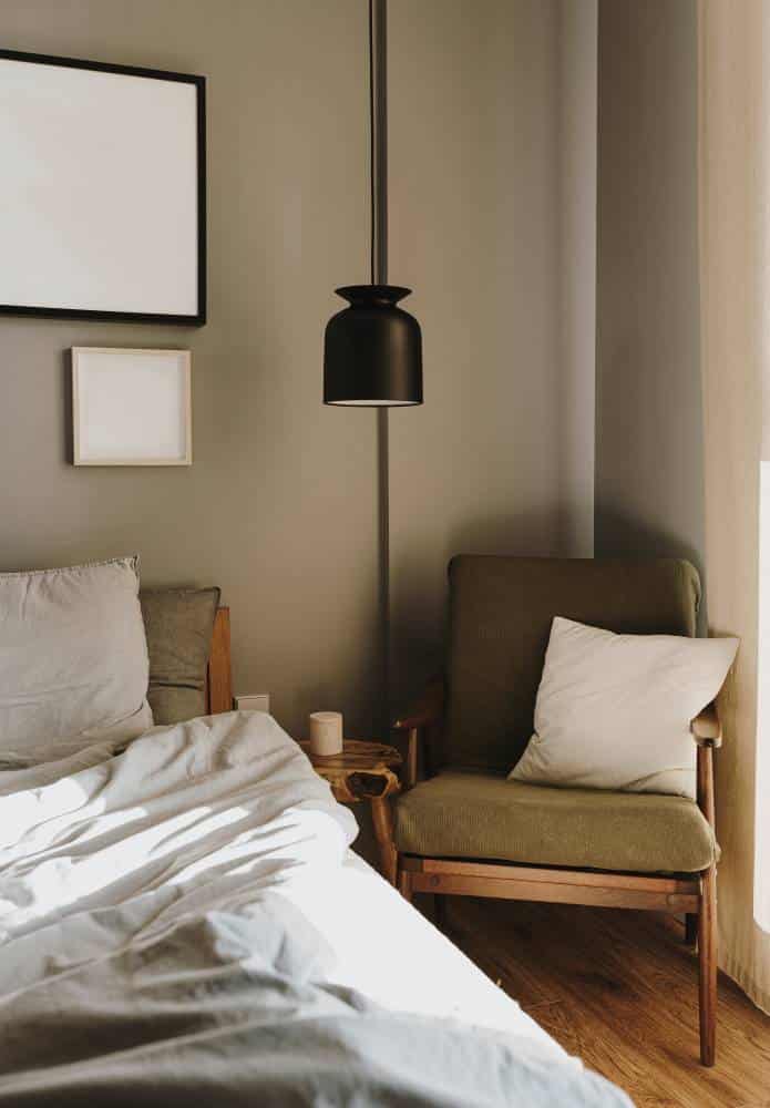 Neutral Scandinavian bedroom with hanging lamp, armchair. Bed with linen cloth. Sunlight shadows