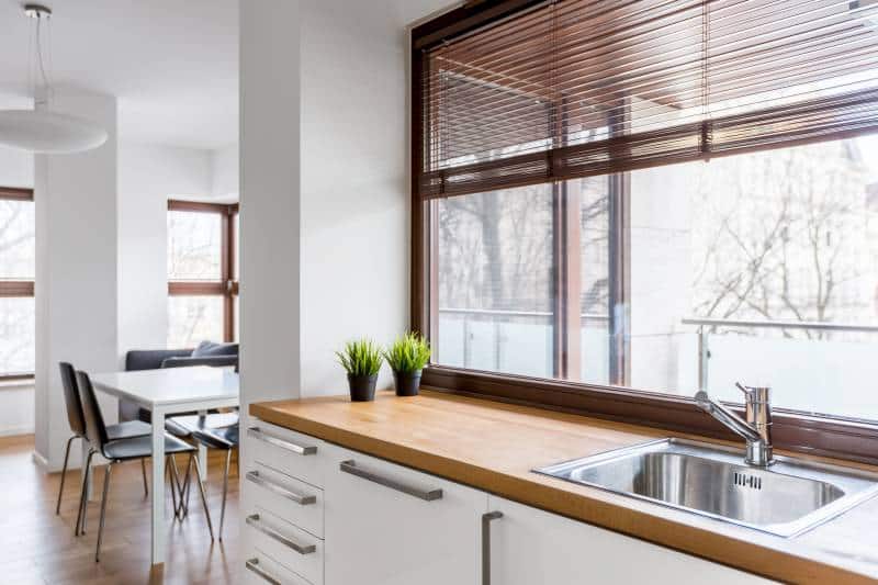 white kitchen with big window with blinds, wooden countertop and silver sink