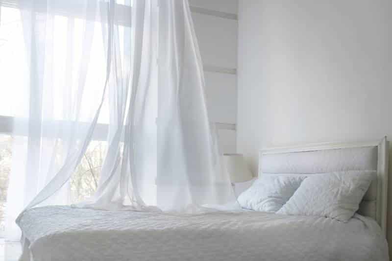 white-themed bed sheets and flowy linen curtain in the morning