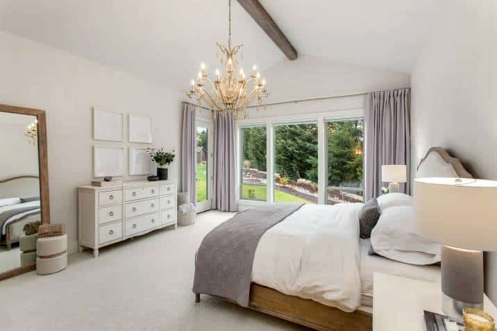 Luxury bedroom features chandelier, wood beam on ceiling, and wall of windows