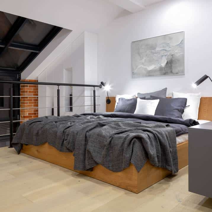 comfortable bed on modern attic bedroom on mezzanine floor in loft style apartment with big window and white walls