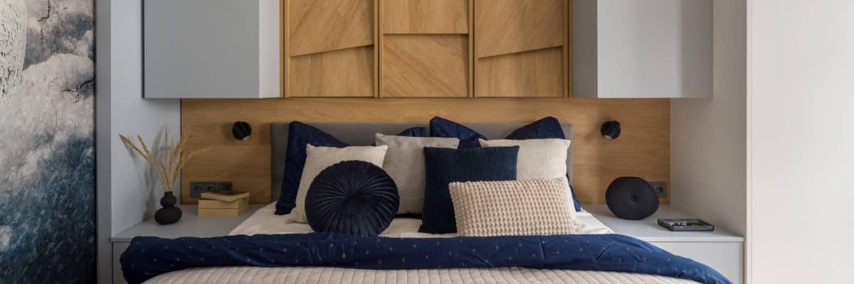 Panorama of modern bedroom with wooden, decorative wall behind cosy bed with stylish bedclothes and two bedside tables with decorations