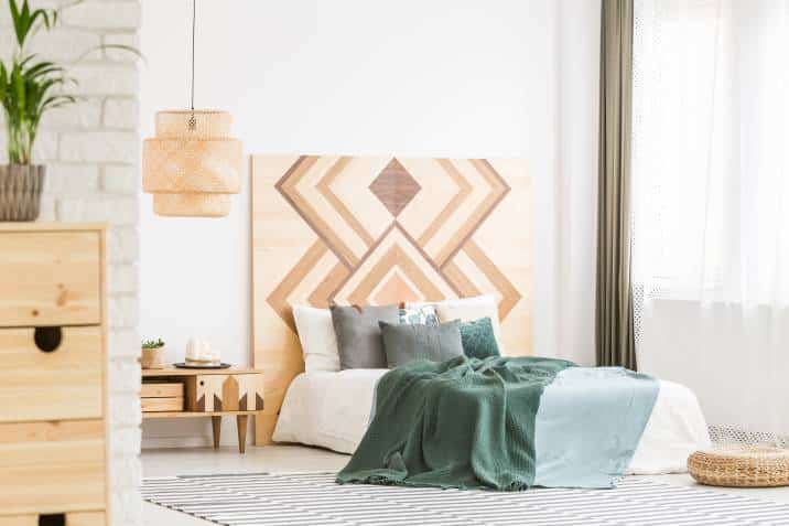 Modern bohemian bedroom. Green bedding on bed against wooden geometric board in natural bedroom with rattan lamp