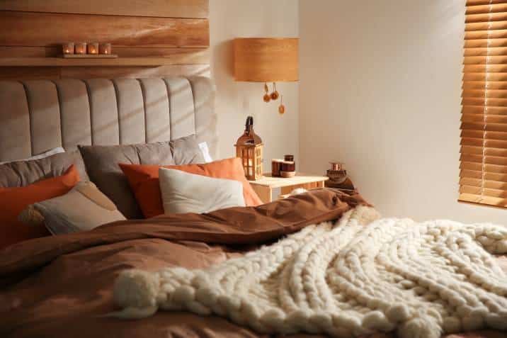 Orange, tan, and white bedroom. Cosy bed with knitted blanket and cushions