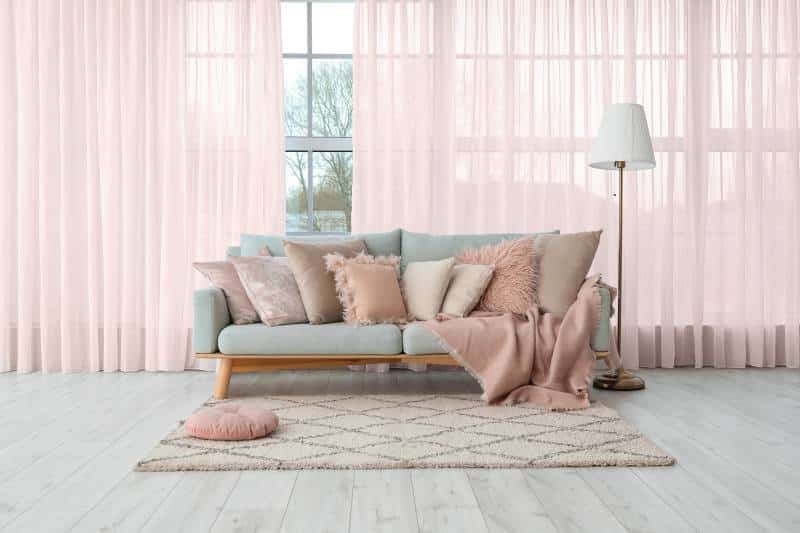 grey sofa with soft pink pillows and lamp, near big window with pink curtains