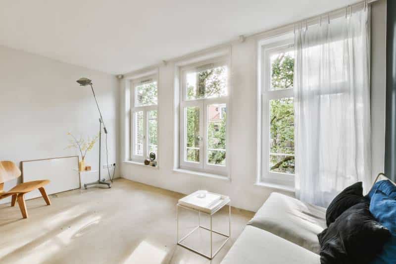 A living room with two large windows covered with sheer curtains. White walls and wood flooring