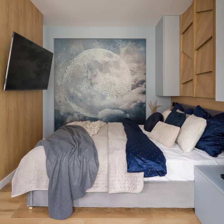 Small bedroom with moon poster. TV on wooden wall and big, comfortable and stylish decorated bed