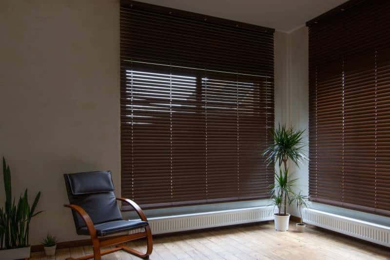 Smart wooden blinds on large windows interior. Living room with armchair and houseplants near windows