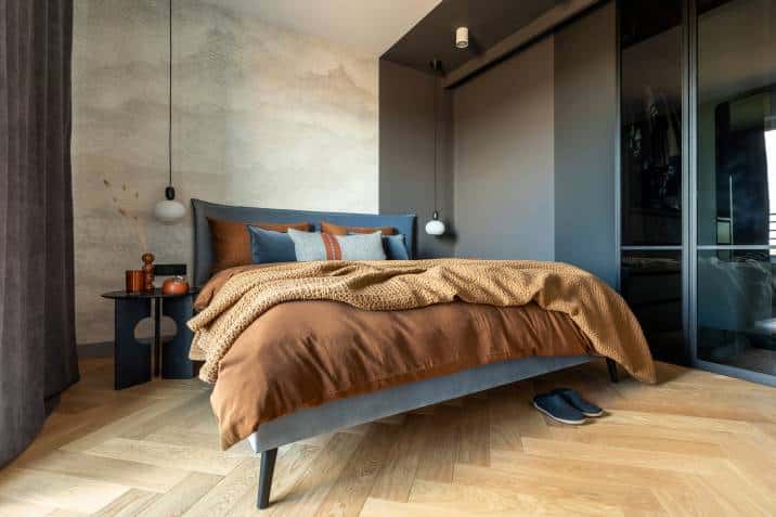 Bed, creative sculptural bedside table, handing lamps on each side of bed. Concrete wall, wooden floor 