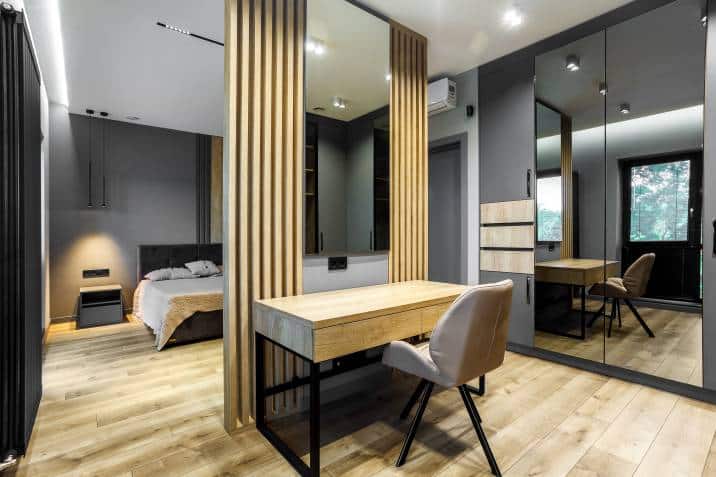 Modern luxury bedroom with wall panel separating a work desk. Loft style with dark and grey colours, dark headboard, wooden floor 