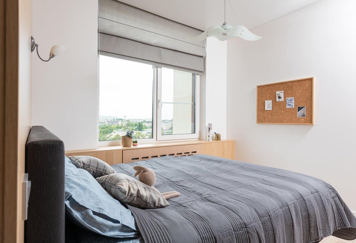 bed with grey linen and a white butterfly pendant light above it