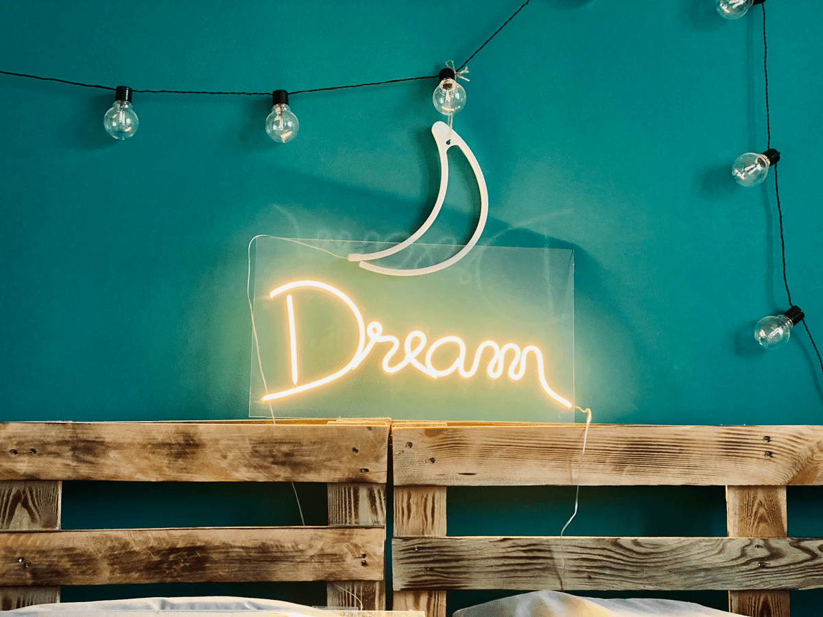 a pallet headboard with a neon sign spelling out "Dream" above it