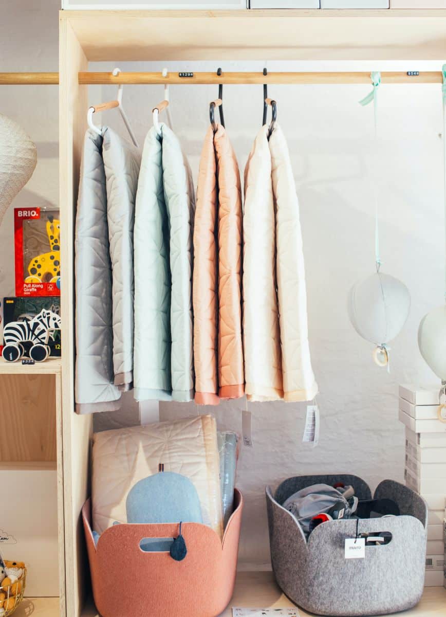 Storage baskets made of felt fabric. The containers sit on a shelf under hanging clothes.