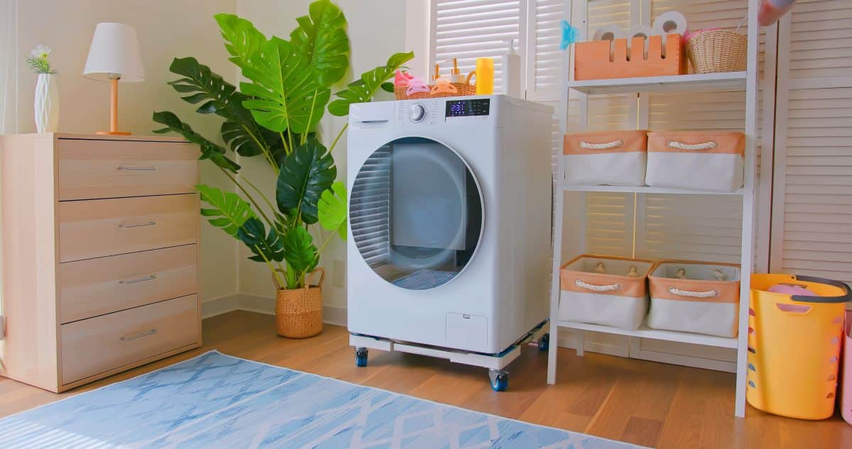 Fabric containers with rope handles on shelf beside modern washing machine 