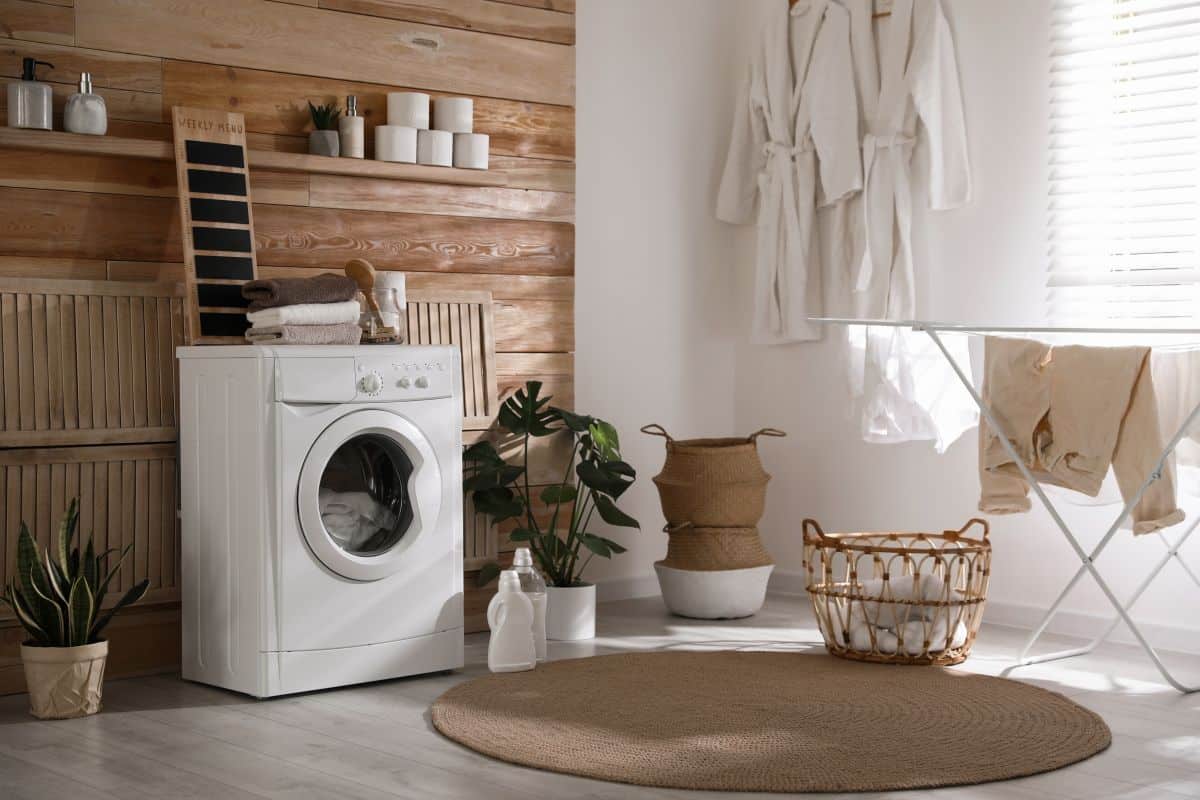 Farmhouse-style laundry room with hanging shelves, rattan baskets, and woven rug 