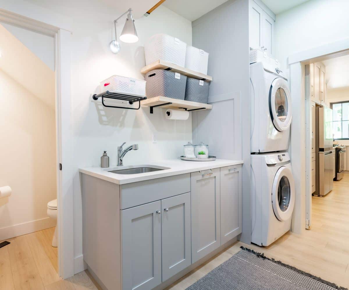 Two layers of floating shelves with plastic containers above the laundry room sink. Stacked washer and dryer beside counter