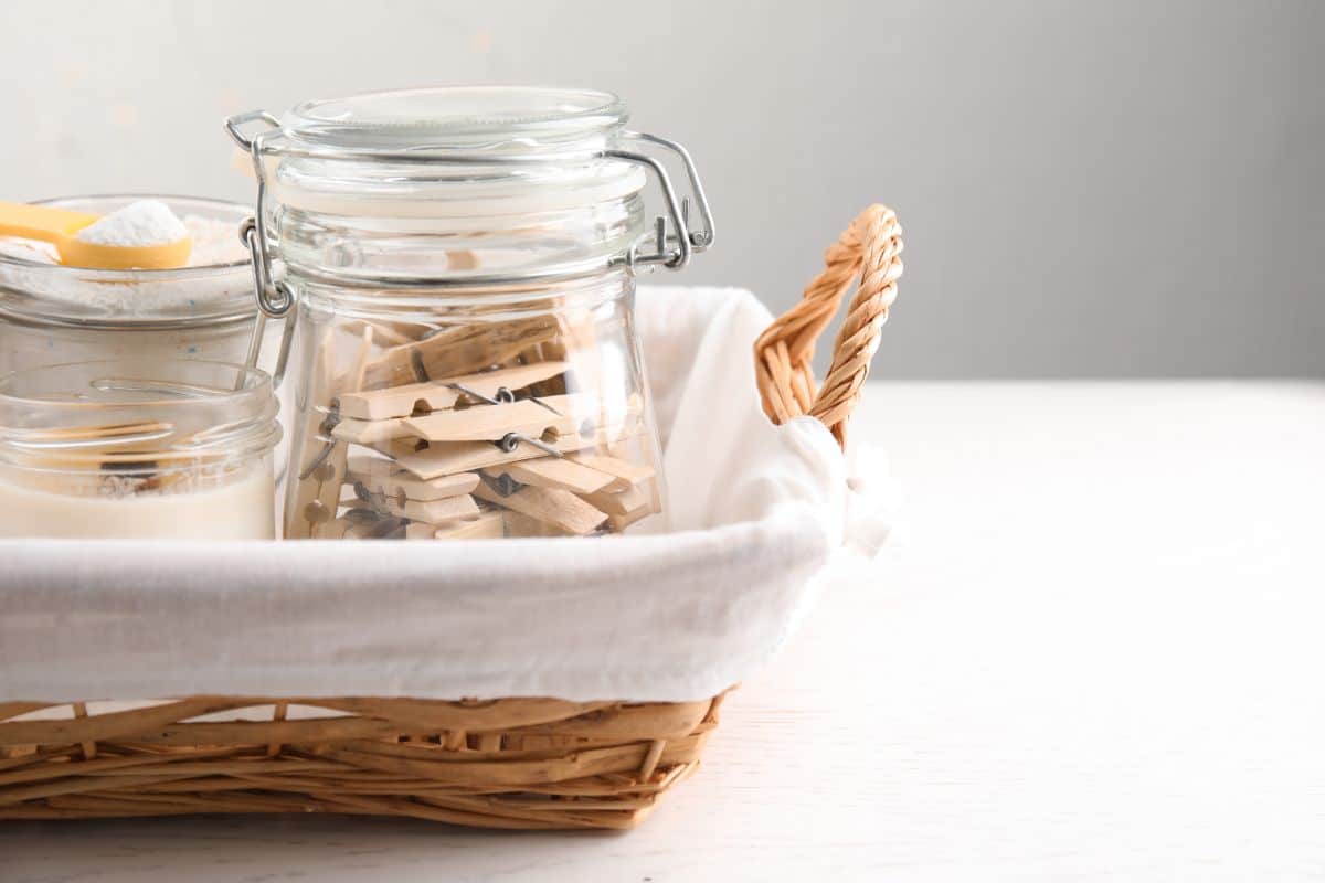 Glass jars with many wooden clothespins and laundry powder in a wicker basket on table