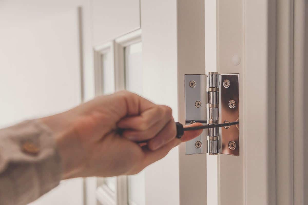 Man repairing a white door. Twists self-tapping screw on stainless door hinge with a screwdriver